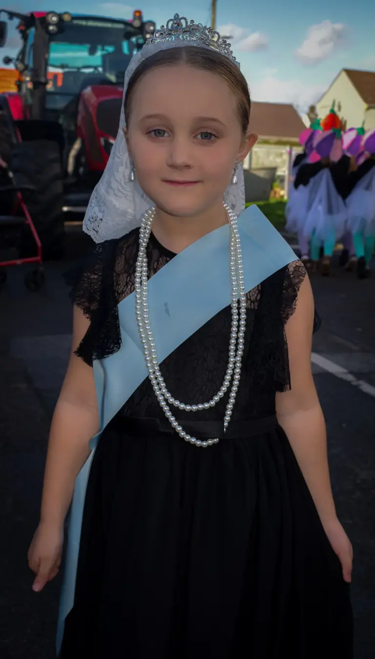 Young girl in a tiara, lace veil, pearls and sash on the carnival queen's float