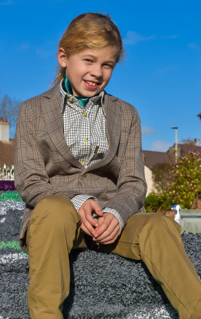Smiling boy in a tweed jacket sitting on the carnival queen's float