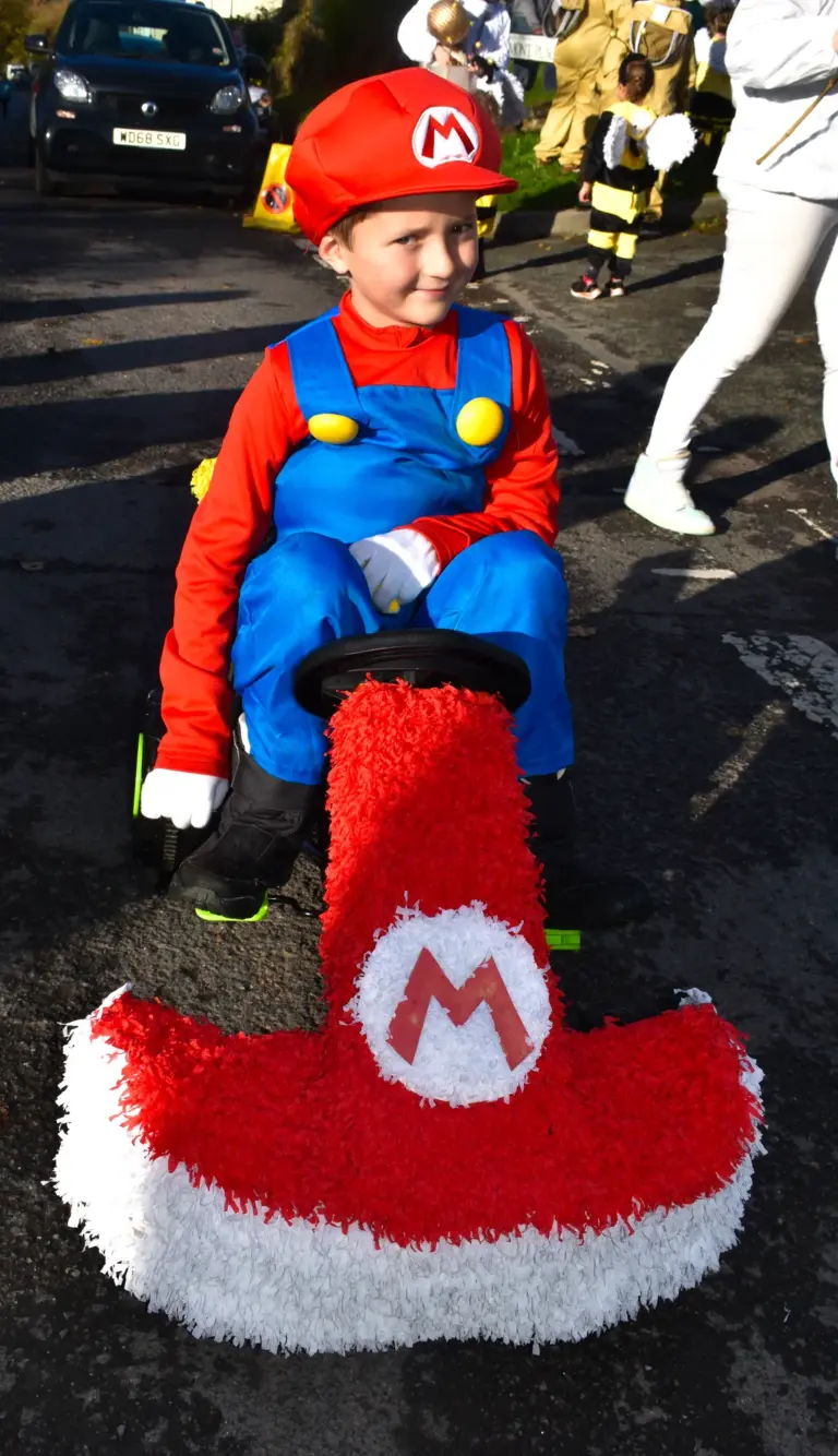 Child dressed as Mario driving a red crepe-paper go-kart