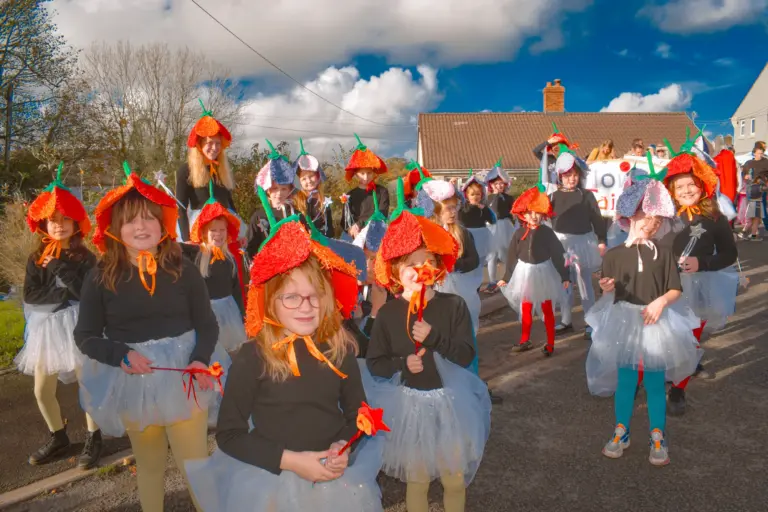 Group of girls in flower hats, black tops and tutus parading through the street
