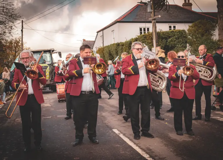 Brass band in red jackets playing trombones and tubas as they march along the street
