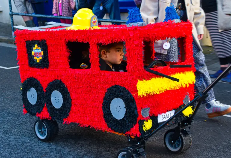 Child riding in a red crepe-paper fire engine built over a pull-along wagon