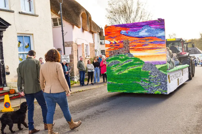 The carnival queen's float with its sunset board passing thatched cottages