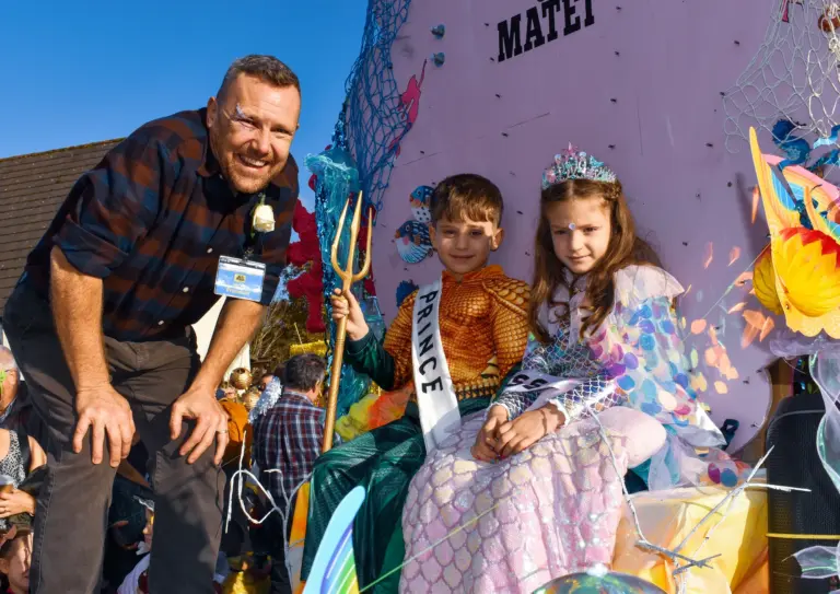 Smiling man crouching beside the carnival Prince and Princess on their float