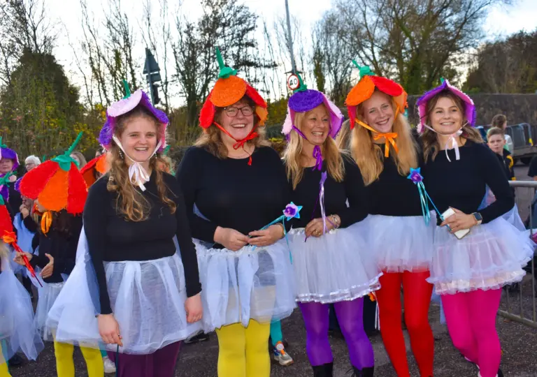 Women in flower hats, tutus and colourful tights laughing as they parade