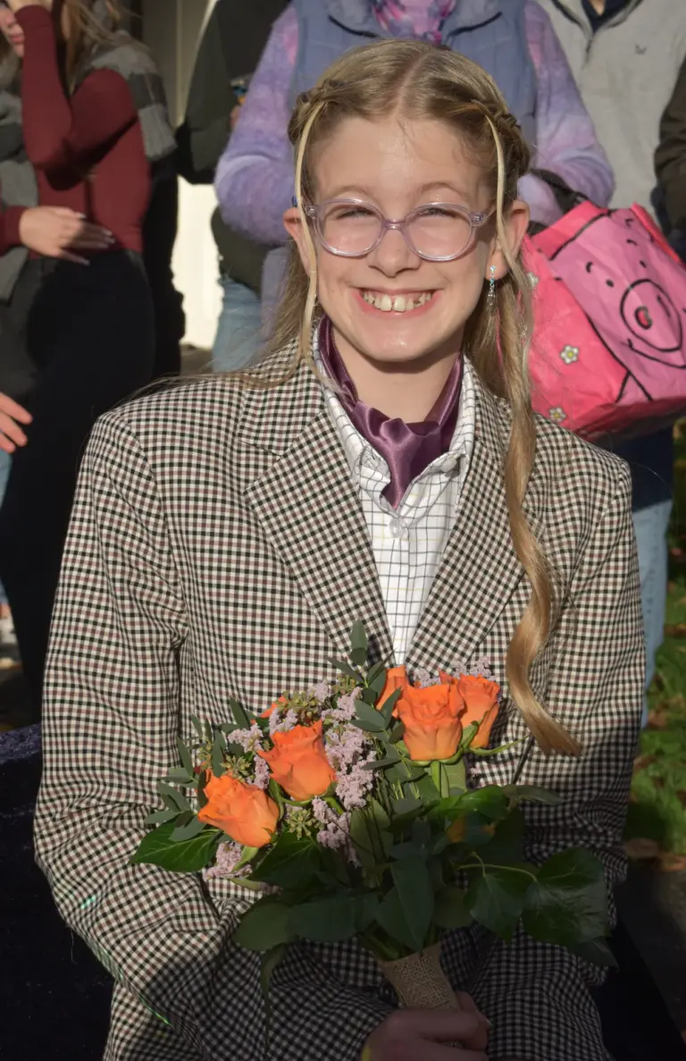 Smiling girl in glasses and a tweed jacket holding orange roses