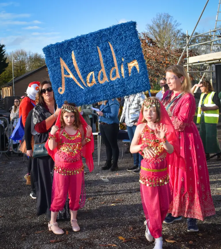 Girls in pink harem costumes dancing behind an Aladdin banner