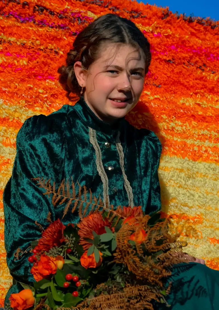 The carnival queen in a green velvet gown holding a bouquet against orange crepe paper