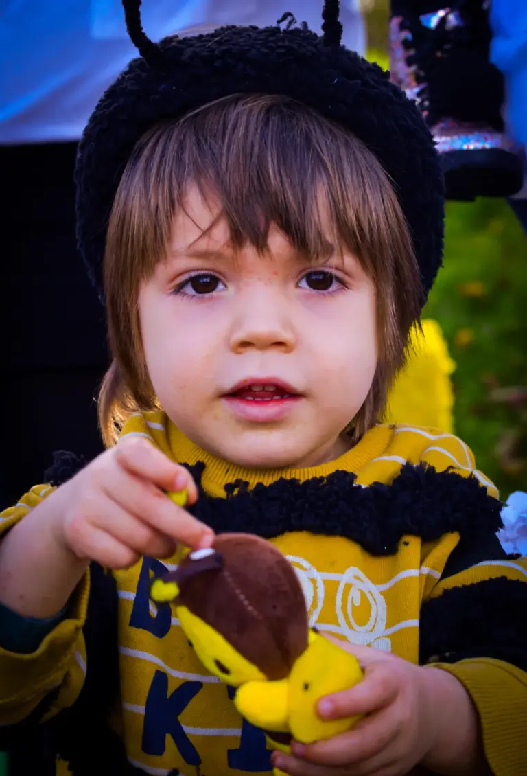 Toddler in bee antennae holding a toy at the afternoon parade