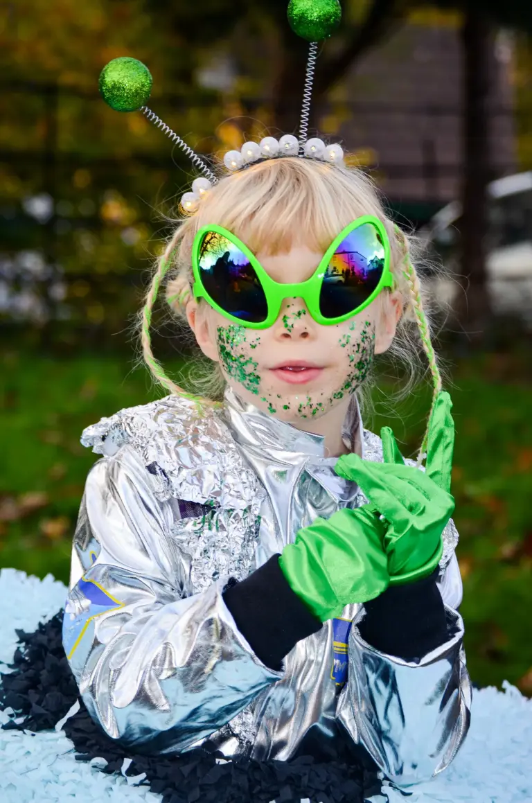 Child dressed as an alien with green glasses, antennae and a silver jacket