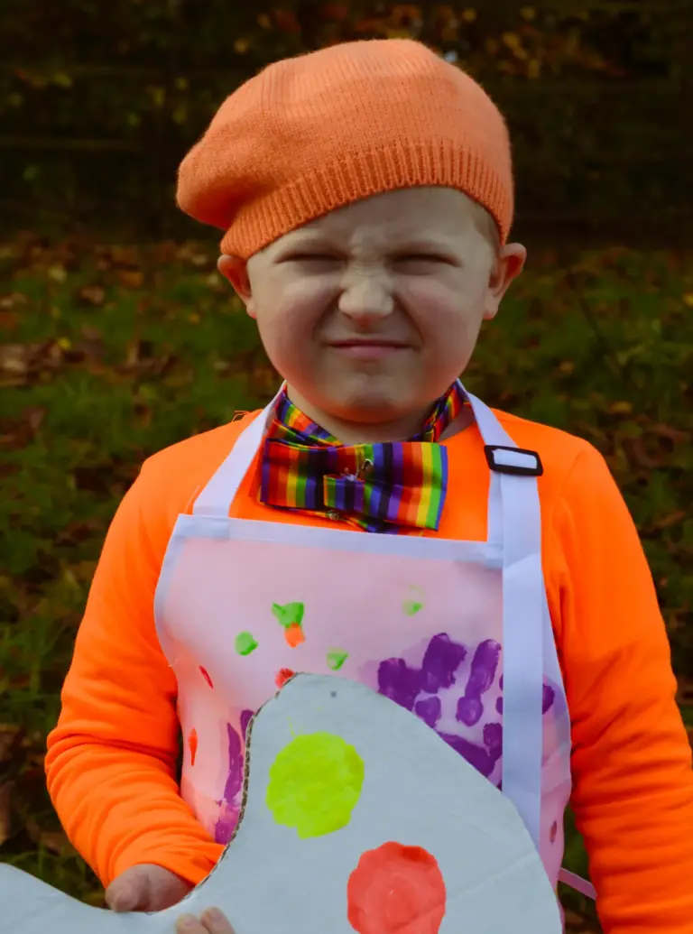 Child in an orange beret and handprint apron pulling a cheeky face