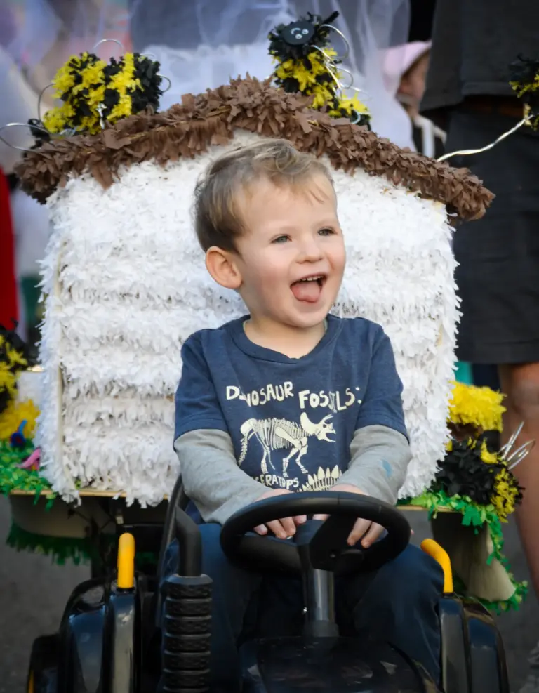 Laughing toddler driving a ride-on car decorated as a beehive