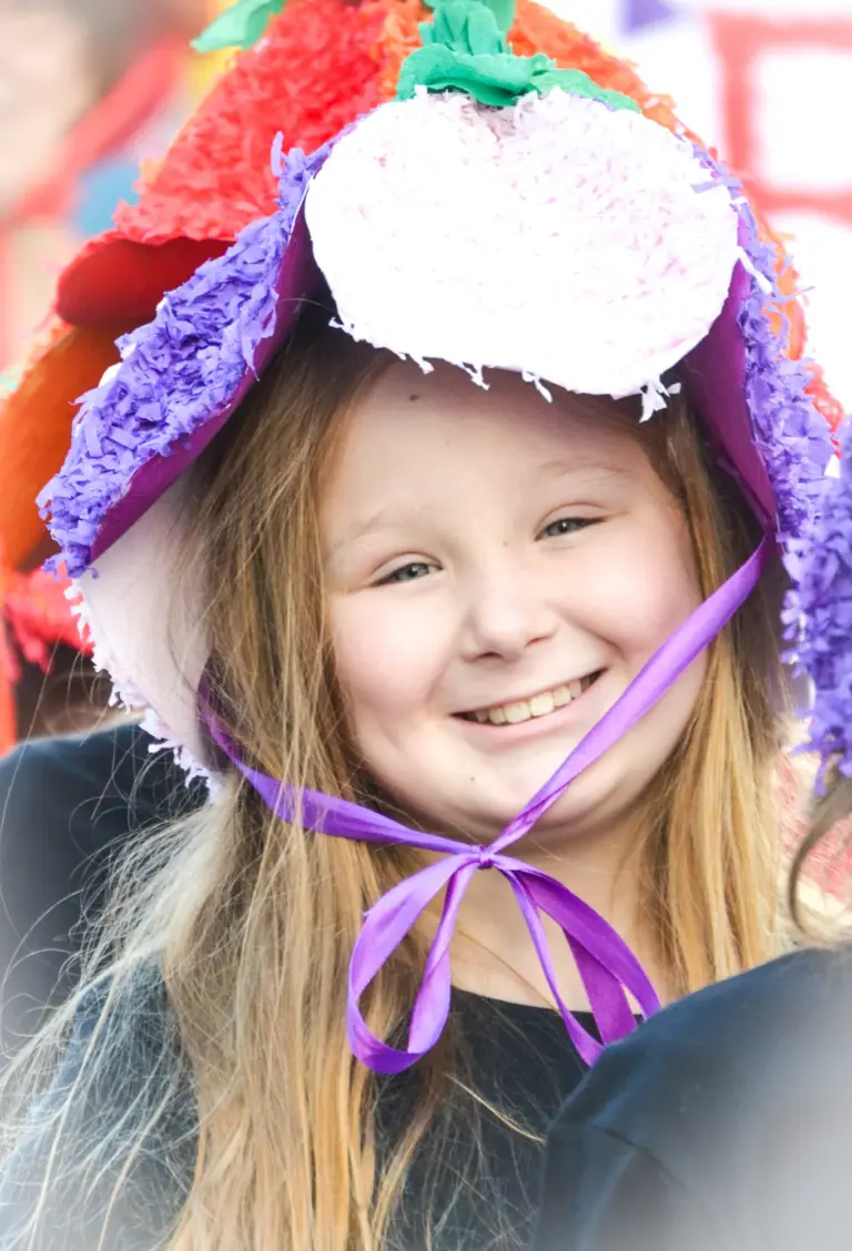 Smiling girl in a crepe-paper flower bonnet tied with a purple ribbon