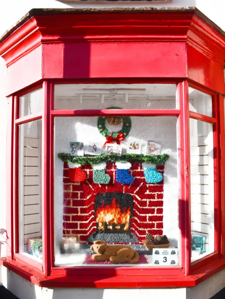 Red phone-box style shop window with a knitted Christmas fireplace display