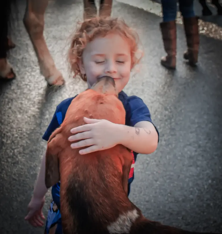 Smiling child hugging a red-brown dog in the street