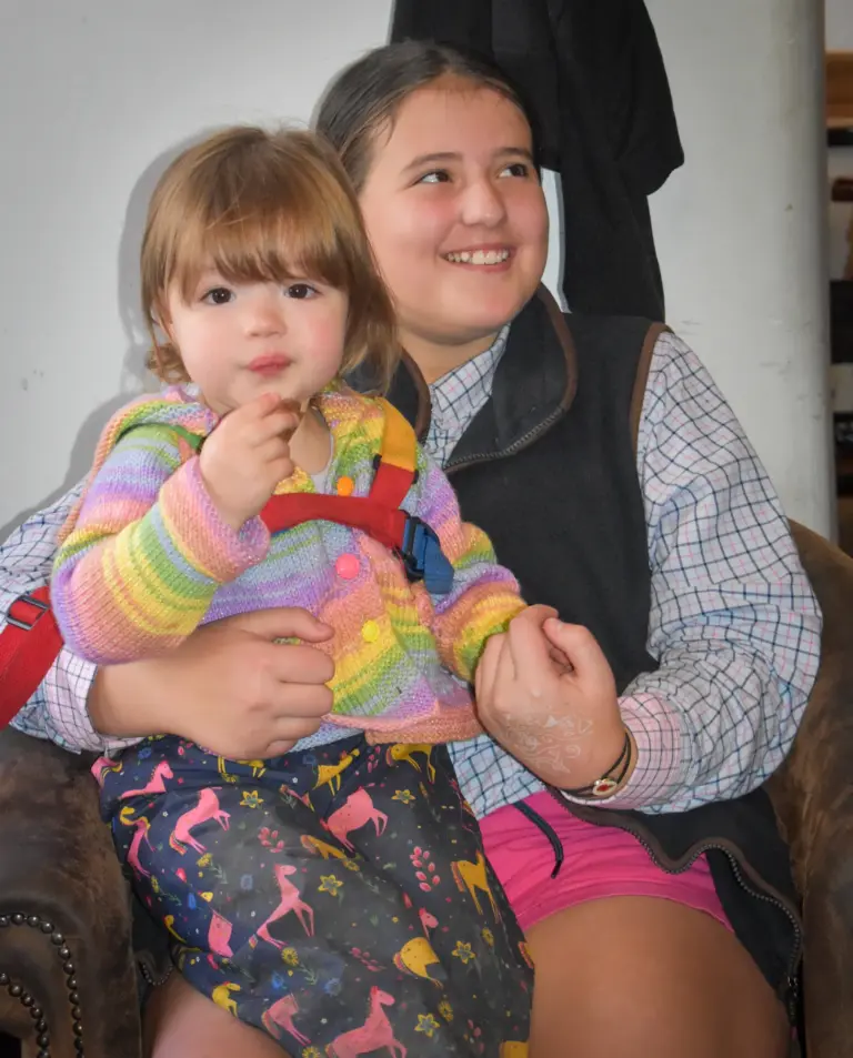 Smiling girl holding a toddler in a rainbow jumper on her lap