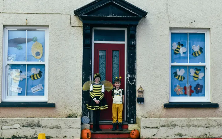 Two children dressed as bees on the doorstep of a house with bee-decorated windows