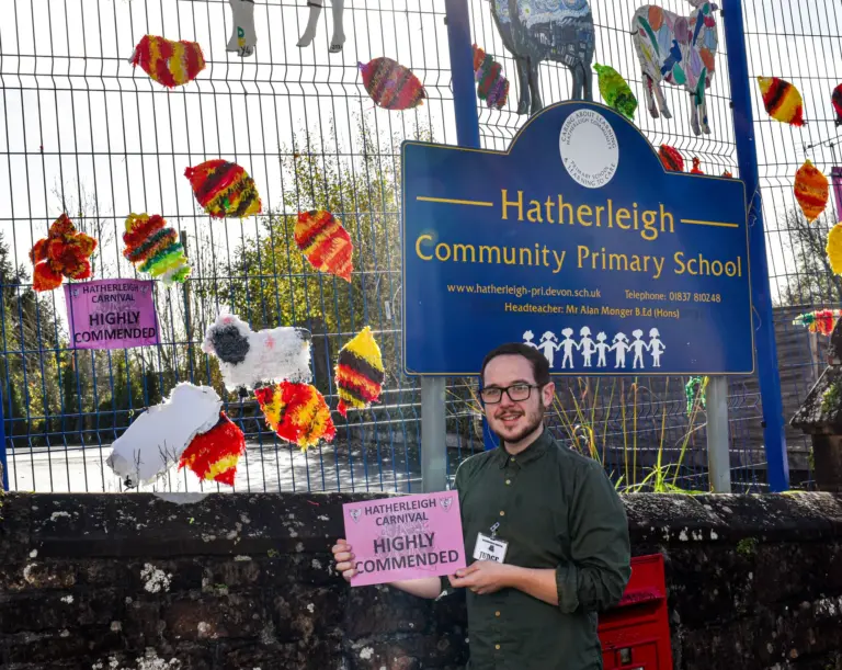 Teacher holding a Highly Commended card outside Hatherleigh Community Primary School