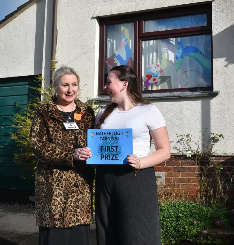 Two women holding a Hatherleigh Carnival first prize card outside a decorated house