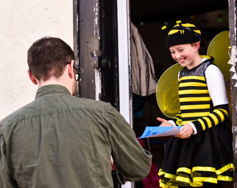 Judge handing a certificate to a girl in a bee costume at her front door