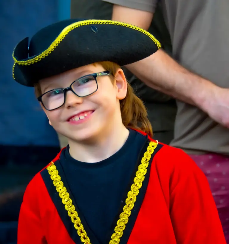 Smiling child in glasses wearing a black tricorn hat and red coat