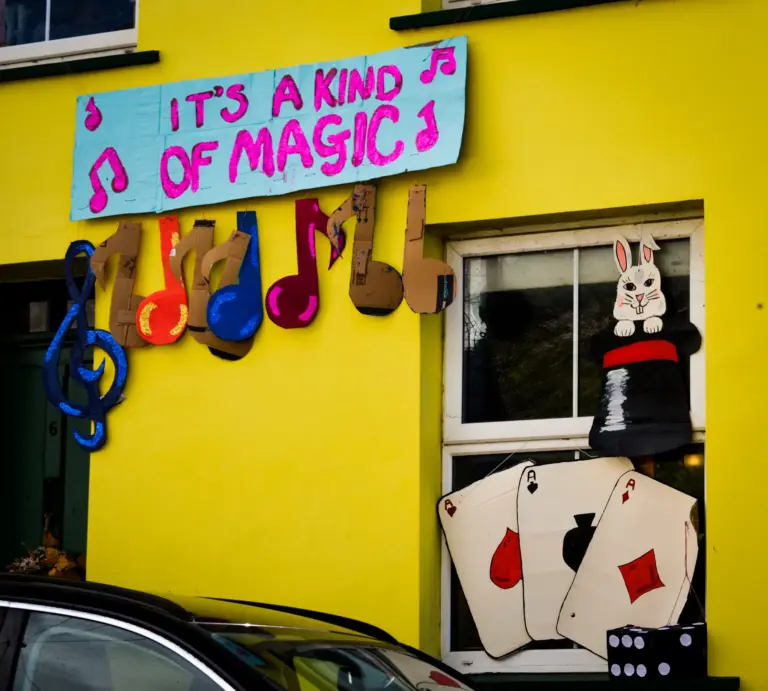 Yellow house decorated with an It's a Kind of Magic sign, musical notes and playing cards