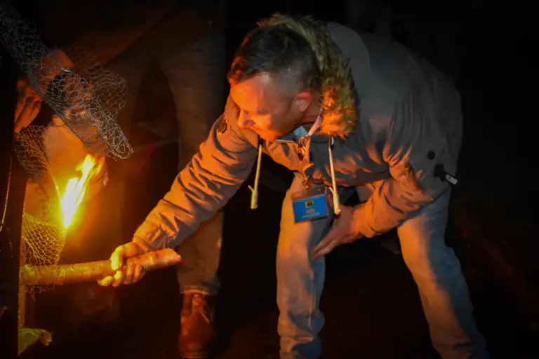 Man in a fur-hooded coat holding a burning torch to light a tar barrel