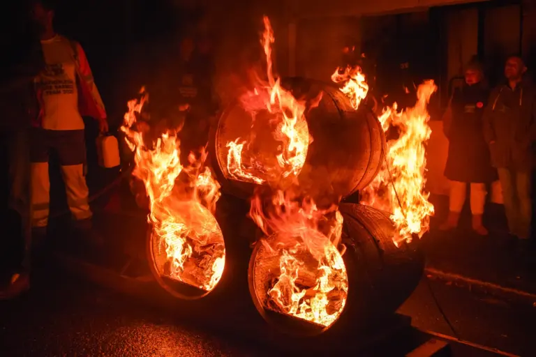 Stacked tar barrels catching fire on their sledge with bright orange flames in the dark