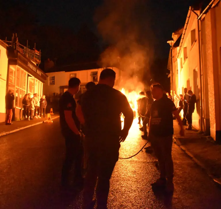 Team pulling flaming barrels down the high street past onlookers