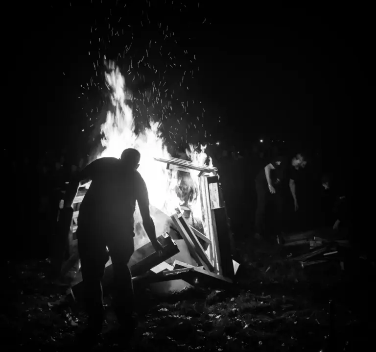Black and white photo of a figure silhouetted against the blazing bonfire