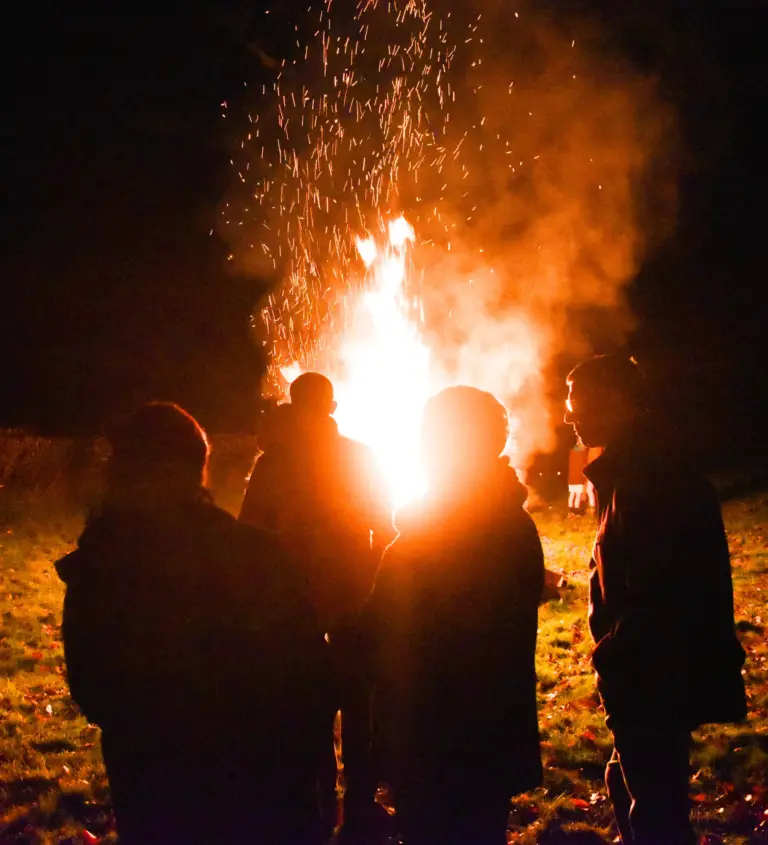 Onlookers silhouetted against the bonfire as sparks shoot skywards