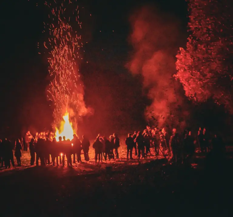 Wide shot of the crowd gathered around the bonfire with sparks and smoke rising