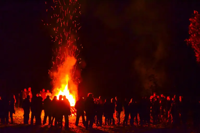 Crowd silhouetted against the blazing bonfire as a column of sparks shoots into the dark sky