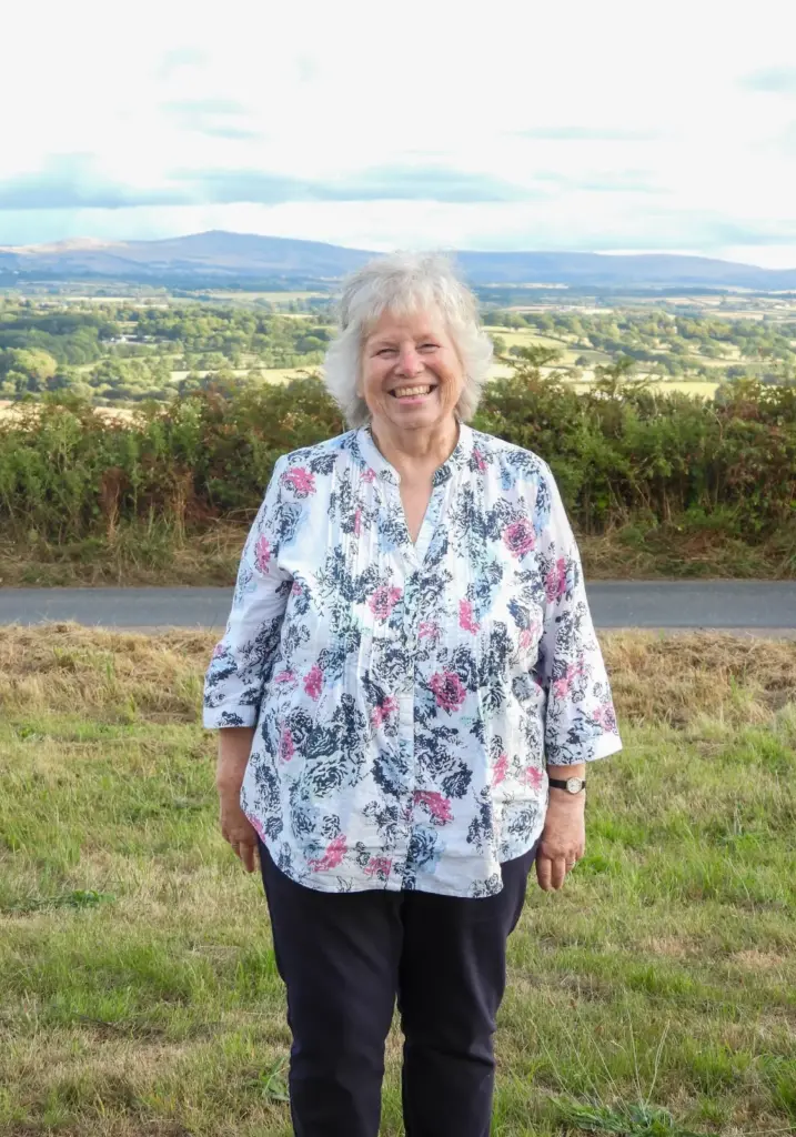 Monica Jones, Hatherleigh Carnival President 2026, smiling broadly in a floral blouse with Dartmoor in the distance behind her