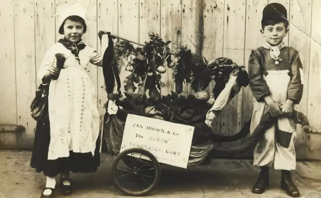 Archive photo of two children in Dutch costume with a decorated vegetable cart signed Jan Hoorn & Co, The Dutch Vegetable Cart