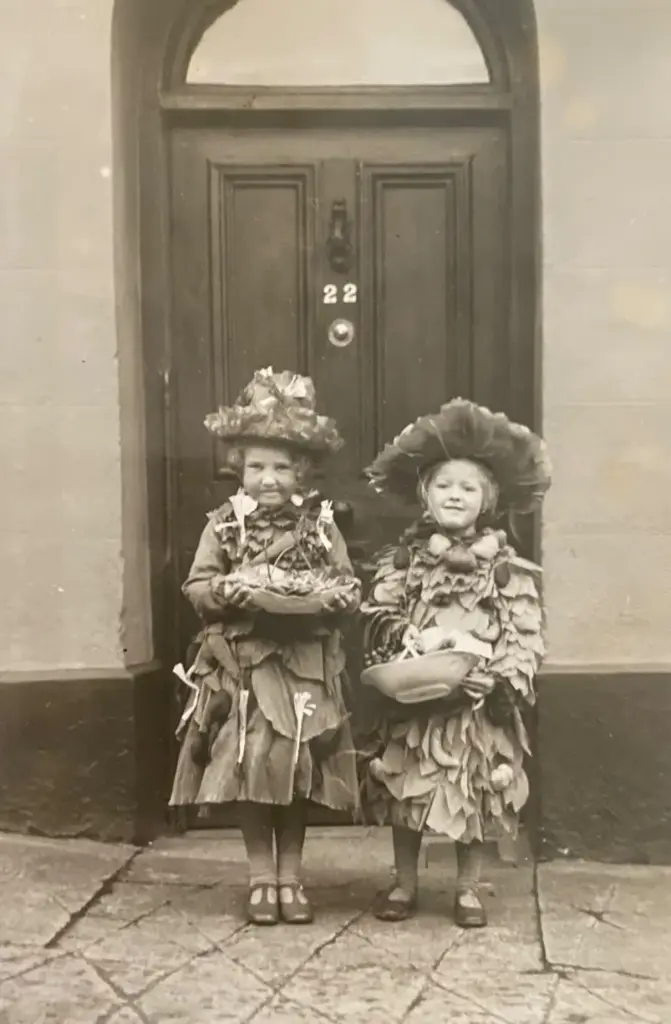 Archive photo of two young girls in costumes made of leaves, standing outside the door of number 22