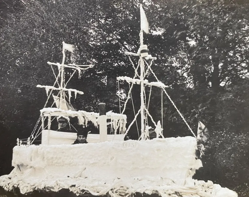 Archive photo of a carnival float built as a white sailing ship with masts and rigging, with two crew aboard