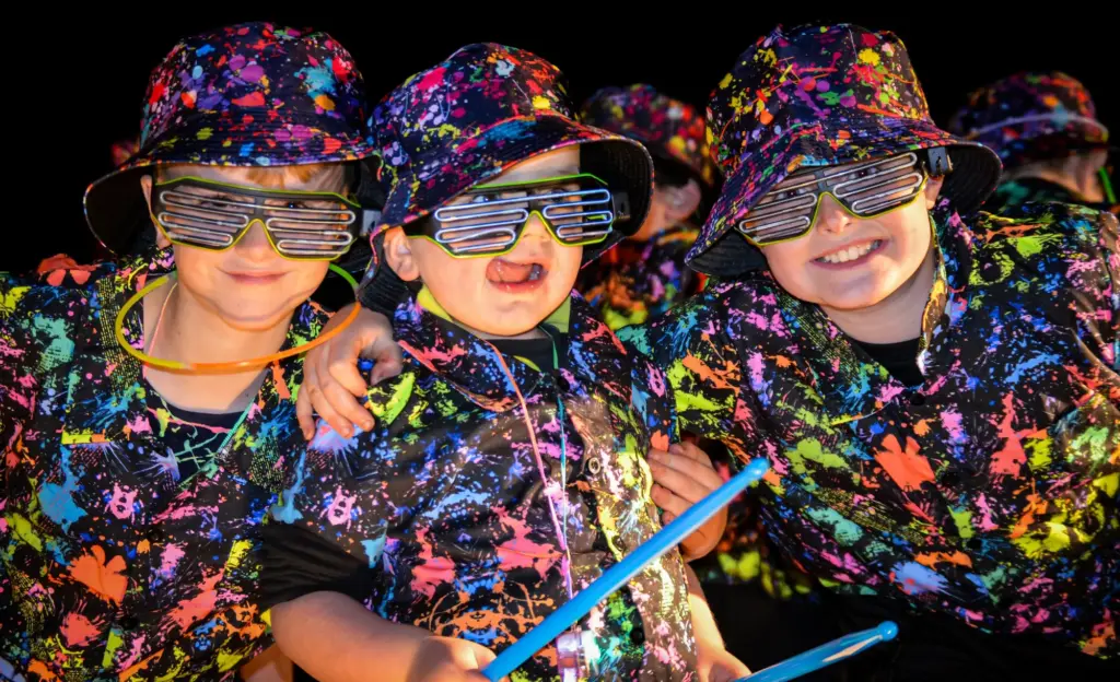 Young carnival-goers in neon paint-splatter costumes, hats and glasses