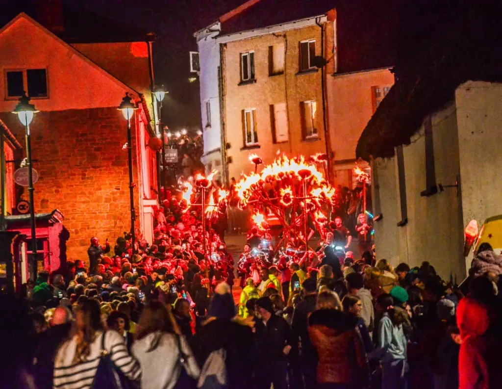 Crowds lining Hatherleigh High Street as the illuminated carnival procession passes at night