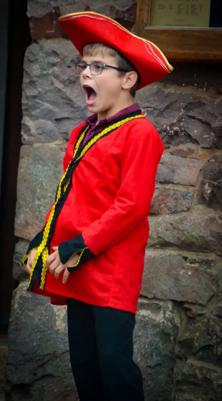 Young town crier in a red tricorn hat and red gold-braided coat calling out in full voice
